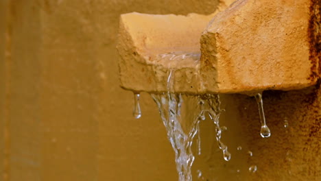 water flowing from a stone gutter on a textured wall, stream of water pouring from a stone spout, water cascading from a concrete channel, water dripping from a rough stone gutter.