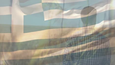 Animation-of-flag-of-greece-blowing-over-male-farmer-standing-in-field-of-wheat