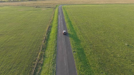 a lone car drives along an empty countryside road bordered by green fields. the peaceful rural scene captures the simplicity and tranquility of open landscapes under clear daylight