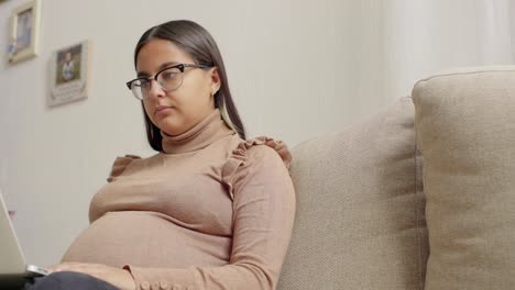 una joven latinx embarazada usando una laptop en la cama 4k