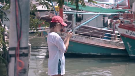 attractive girl in cap holds cellphone against fishing boats