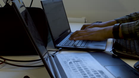 a close up shot of a busy and cluttered work desk of an it professional as he transfers data from one laptop to another while continuing to type on an external keyboard