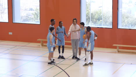 multiracial male basketball players with coach huddling and giving instructions to players in gym