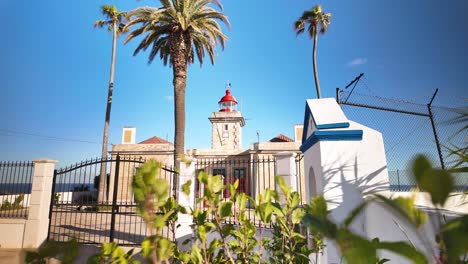 Lighthouse-in-Lagos,-Portugal,-under-a-bright-blue-sky,-surrounded-by-greenery-and-palm-trees,-timelapse