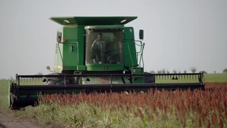 Farmer-on-a-thresher,-or-threshing-machine,-on-a-farm-field,-wide-shot