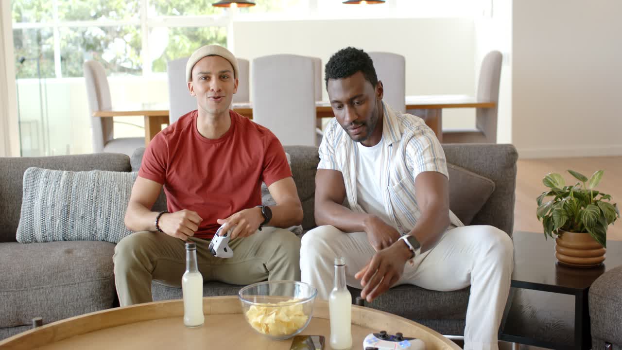 After controller tapping starting match, Diverse male friends gaming and sipping drinks on couch
