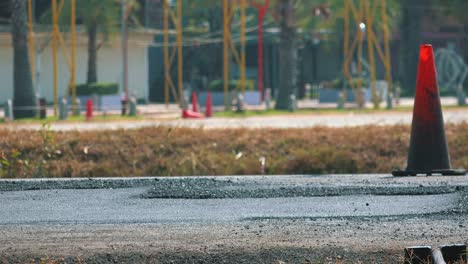 close shot of a steam roller flattening a newly laid road surface by a traffic cone