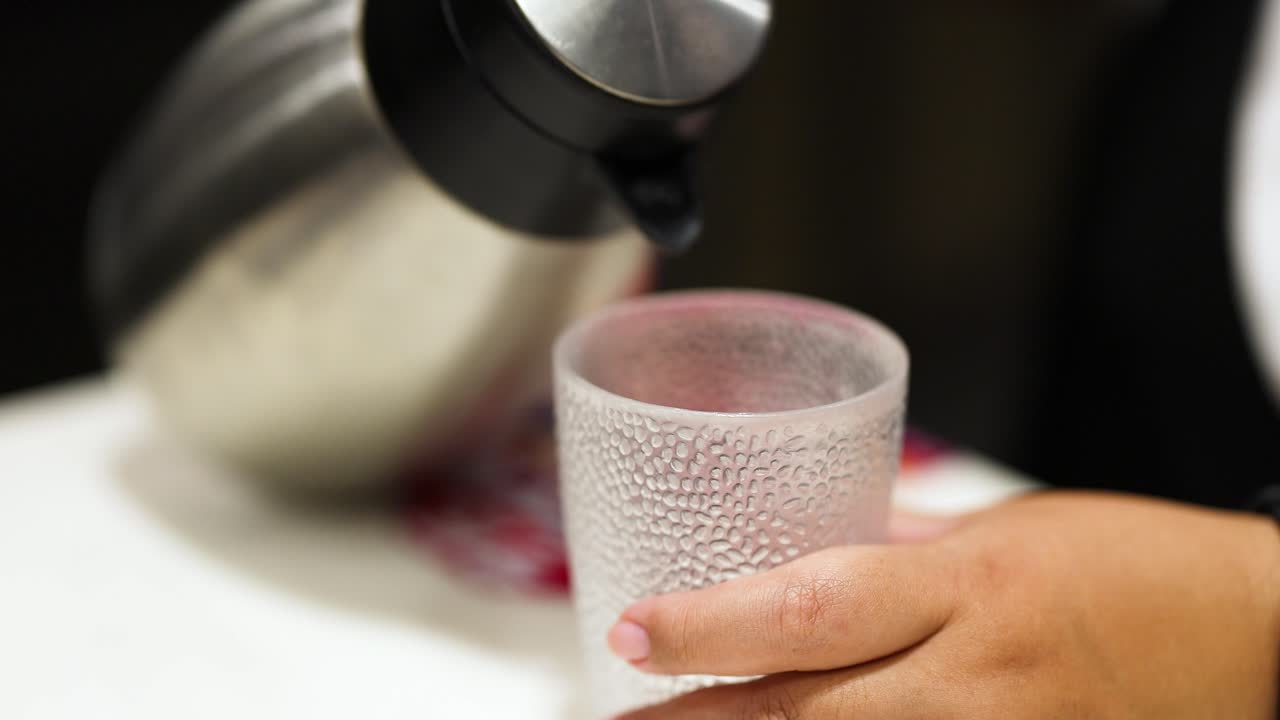 Hand pouring water from kettle into glass