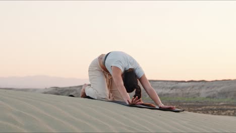 joven morena instructora de yoga calentándose en la arena