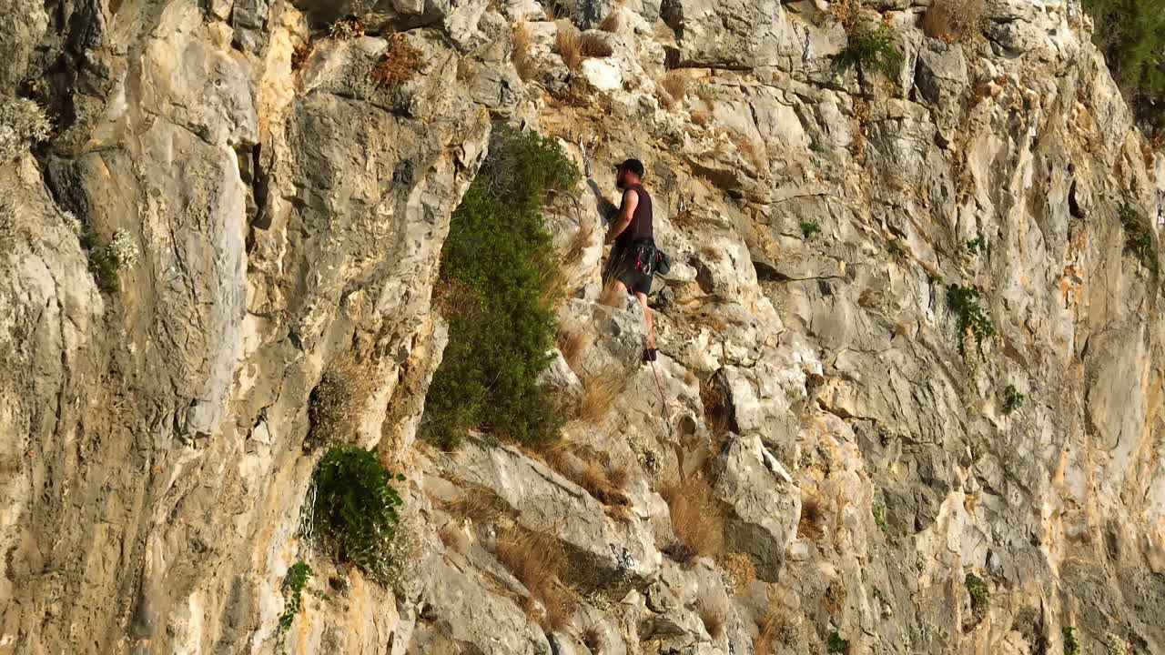 Aerial telezoom circling a mountain climber on a rocky cliff, golden hour