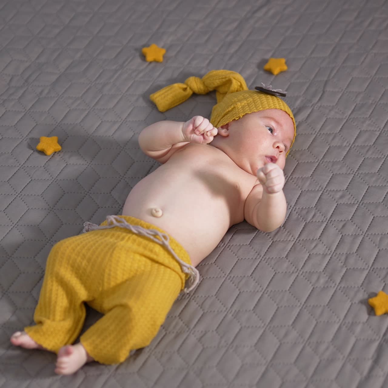 Nice sweet child in yellow funny costume lies on the grey background. Baby moving his lovely little hands actively. Little stars next to the boy
