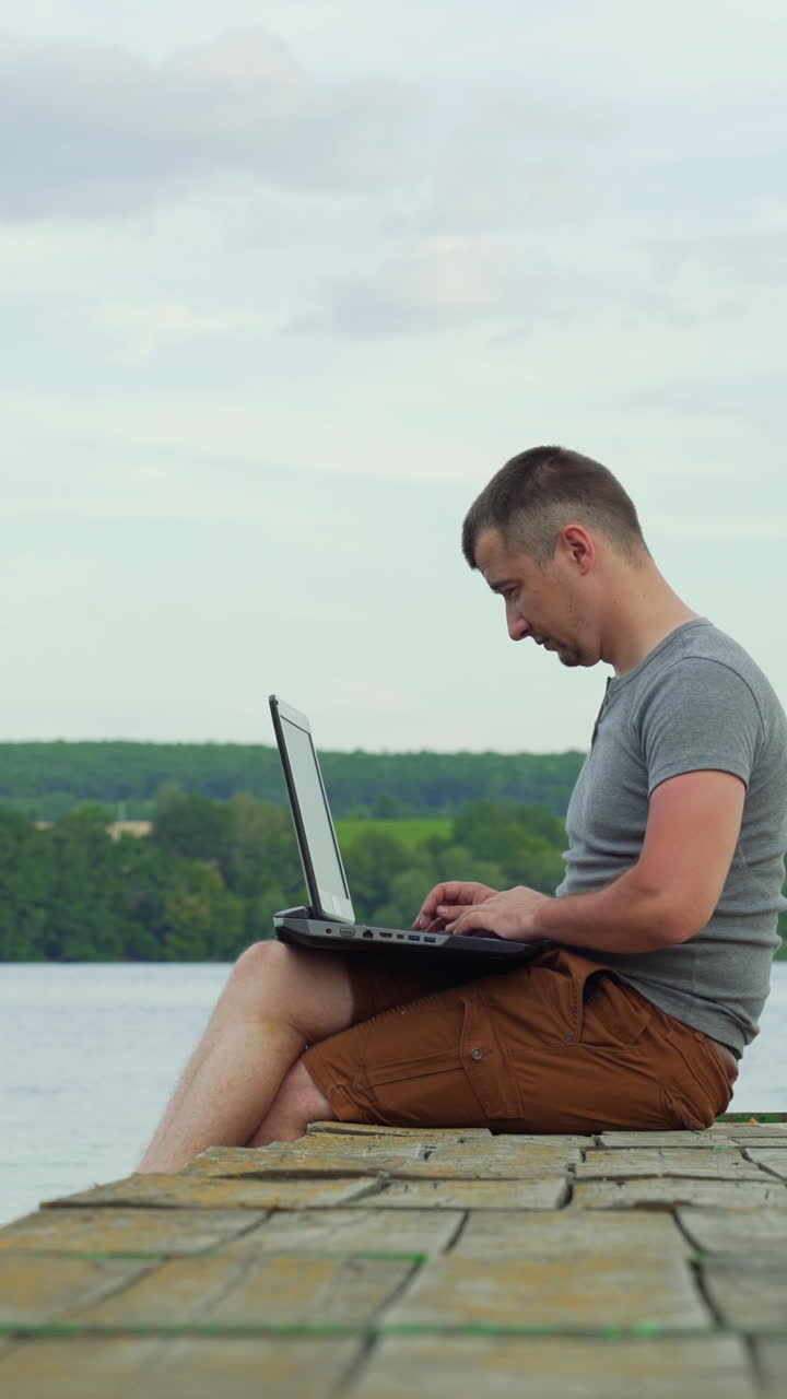 Man on the pier working on a laptop. Work on vacation. Vertical video