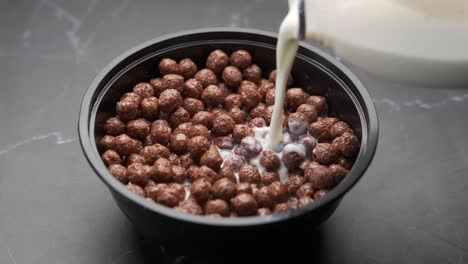 pouring milk over chocolate cereal in a bowl