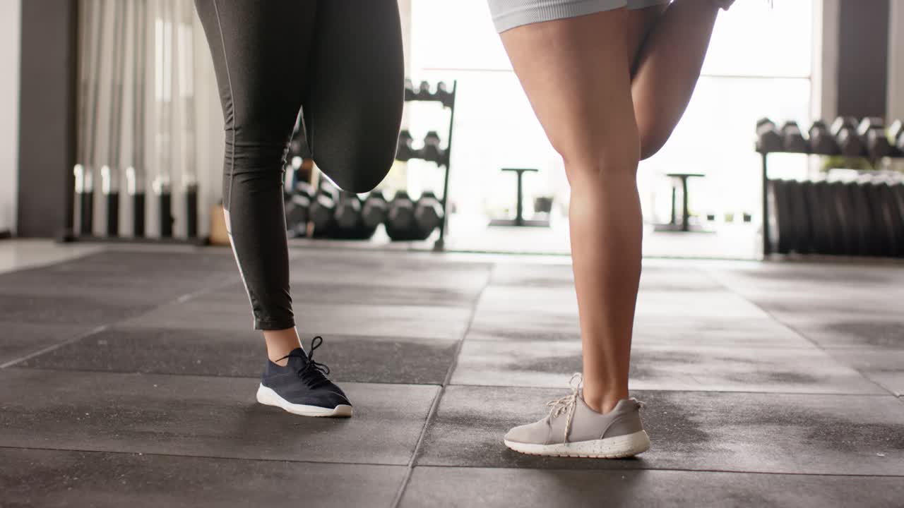 Diverse amiche che eseguono lo stretching dei quadricipiti su un tappetino di gomma nella sala pesi della palestra durante il riscaldamento