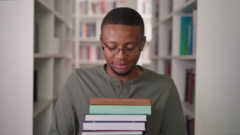maestro negro con pila de libros en la biblioteca. hombre afroamericano lleva libros de texto altos montón a lo largo del pasillo entre el archivo de información. educación escolar