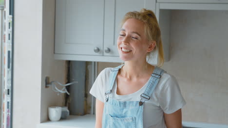 portrait of smiling woman wearing dungarees renovating kitchen at home