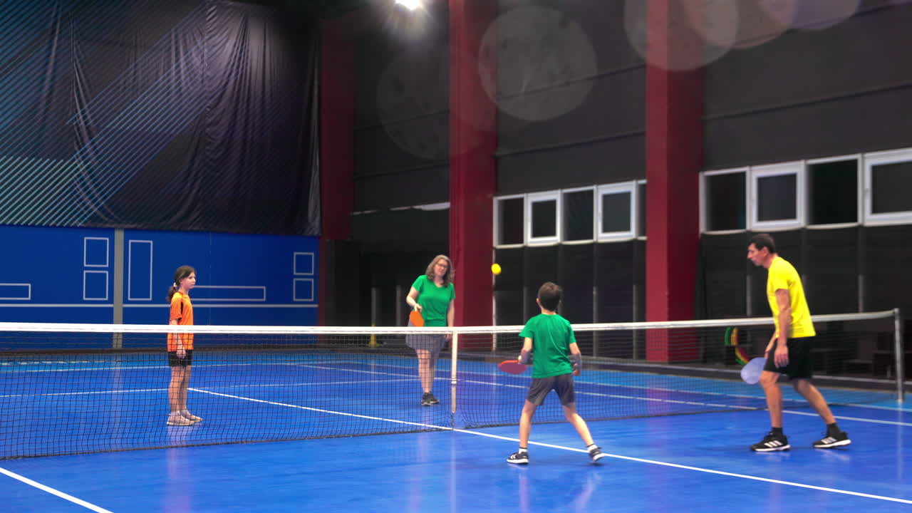 A man teaching his son to play pickleball on a blue, inside court