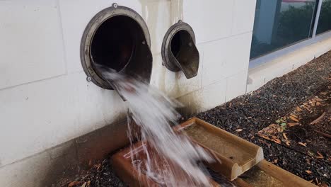 this is a short video of a large amount of water, flowing out of a drainage pipe, on the side of a building, during an afternoon thunderstorm