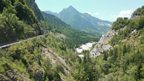 video de drones volando sobre el bosque hasta el puente de la carretera de montaña que se eleva para revelar un valle seco en los dolomitas italianos rodeado de caminos de montaña y acantilados y un pequeño lago debajo