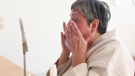 Elderly-woman-in-bathrobe-applying-facial-cream