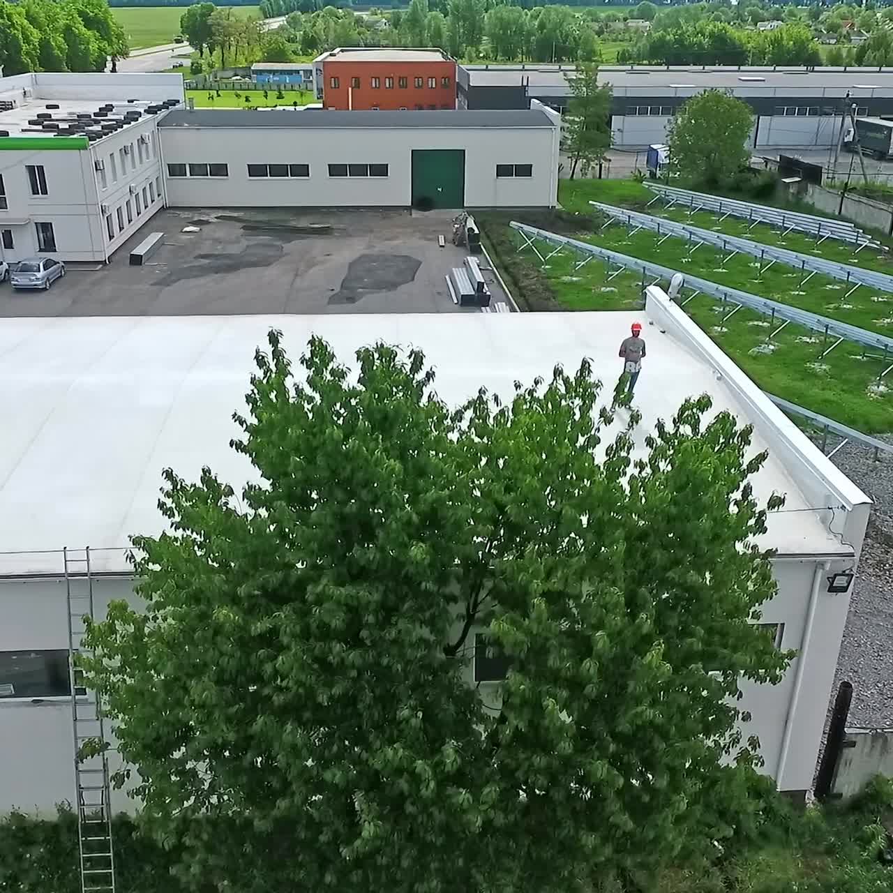 Worker in safety helmet on rooftop. Engineer standing on a flat roof of a big builduing in summer. Development of solar farm from roof. Aerial view.