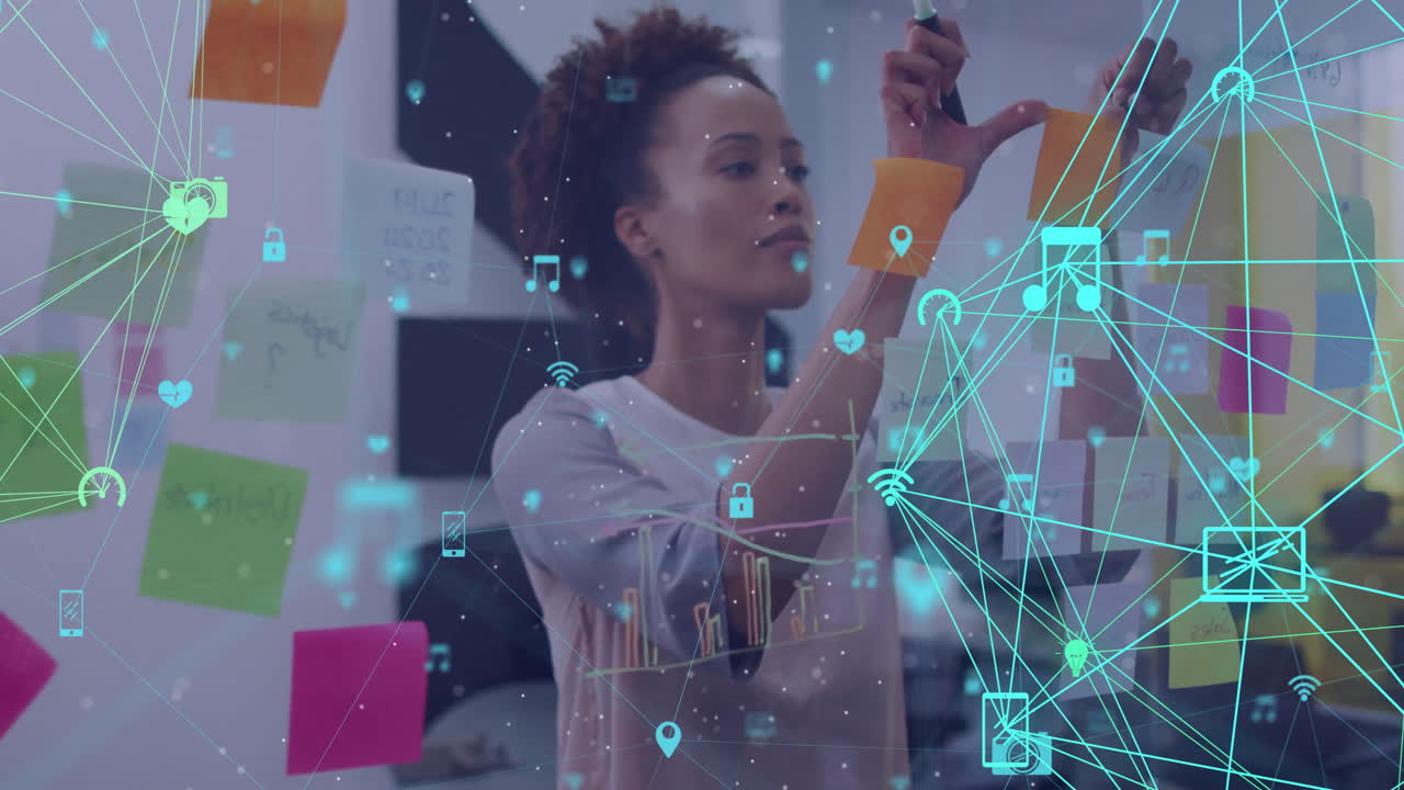 Animation of networks of media icons over biracial casual businesswoman brainstorming at office