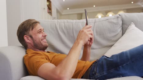 portrait of happy caucasian man lying on sofa using tablet