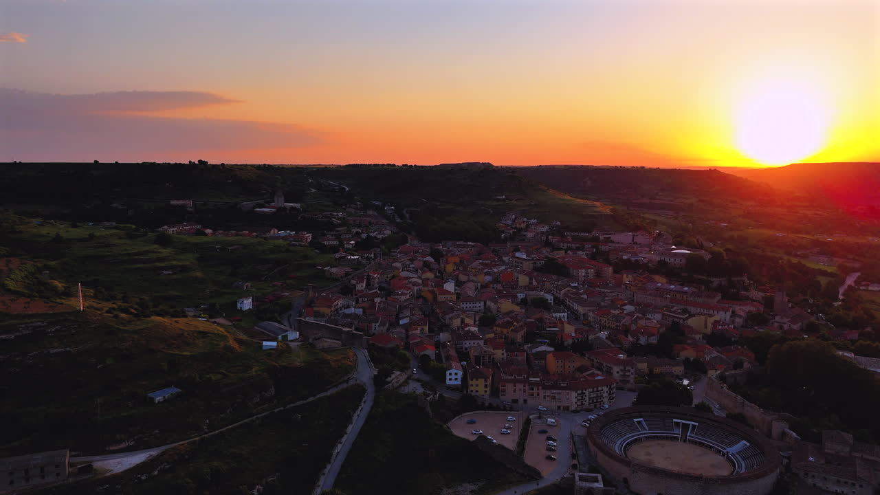 Lateral drone traveling shot over Brihuega, Spain, at sunrise. The clip captures the village rooftops, bullring and rural landscape under golden light, creating a scenic and atmospheric view