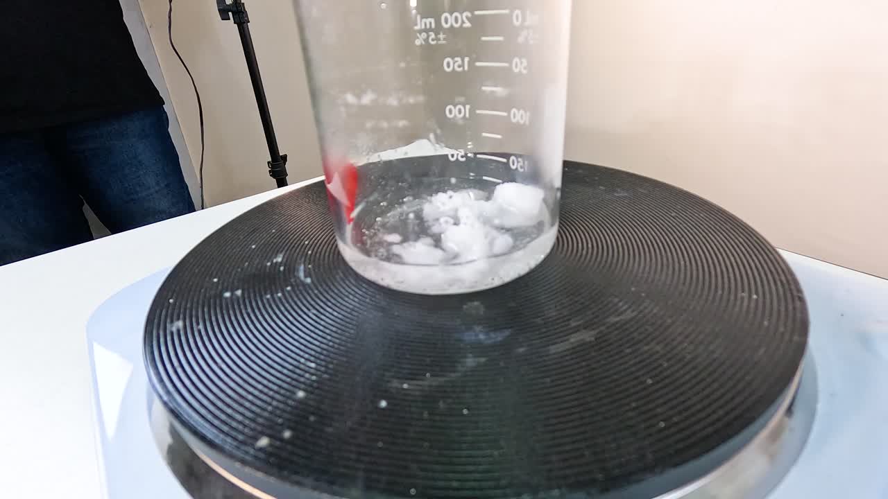 Sodium acetate crystallization process in a beaker on a hot plate, demonstrating chemical reactions and crystal formation