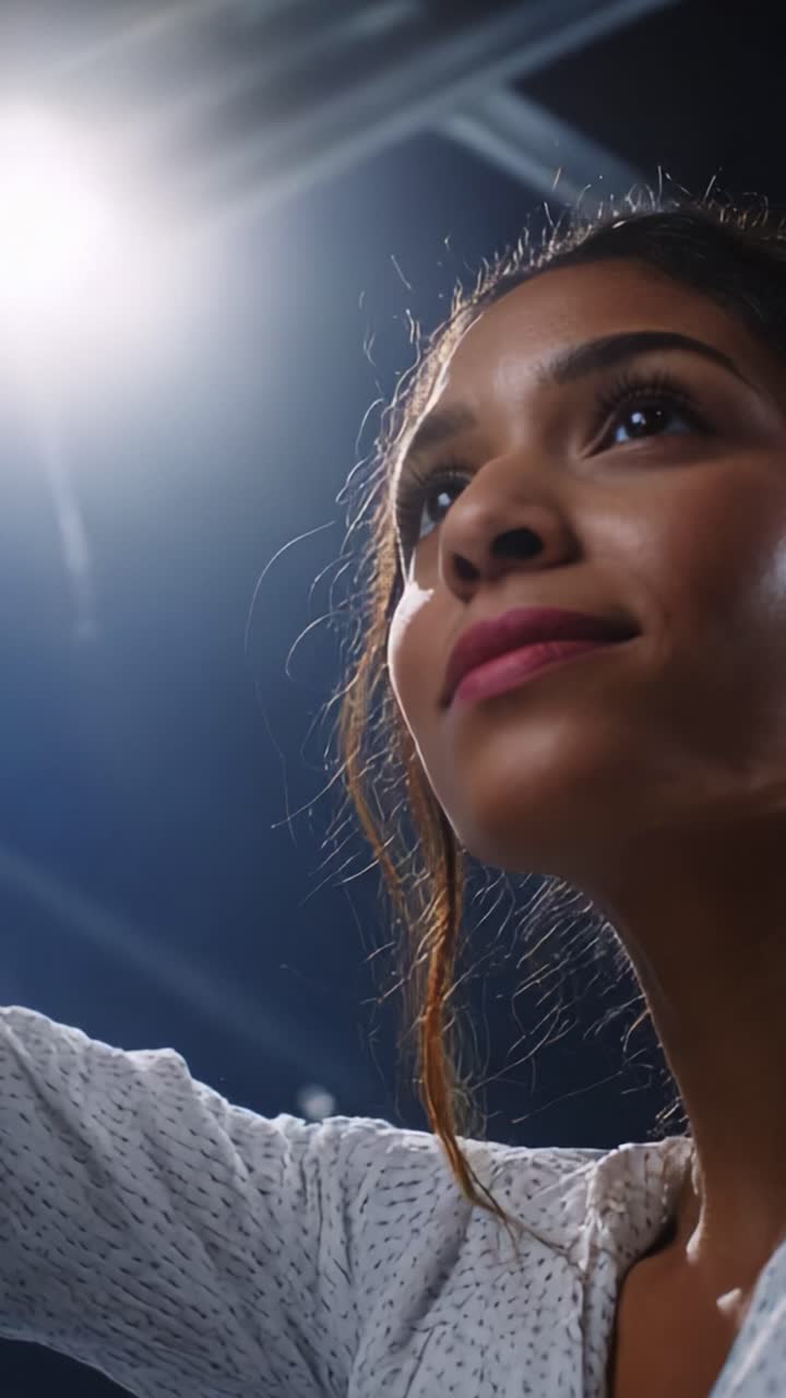 A young woman gazes upward with hope and determination, captured in a moment of inspiration as light illuminates her features, showcasing her focus and positive energy in a studio setting
