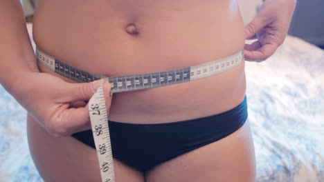 a woman measuring her waist size in centimeters with a measurement tape