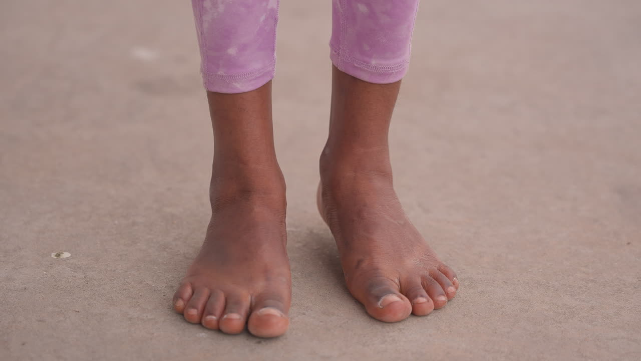 Piedi ricoperti di sabbia che camminano per terra, leggings viola risvoltati, granelli attaccati alla pelle e alle piante, passi fermi e leggero ondeggiamento, atmosfera estiva spontanea di esplorazione e movimento spensierato.