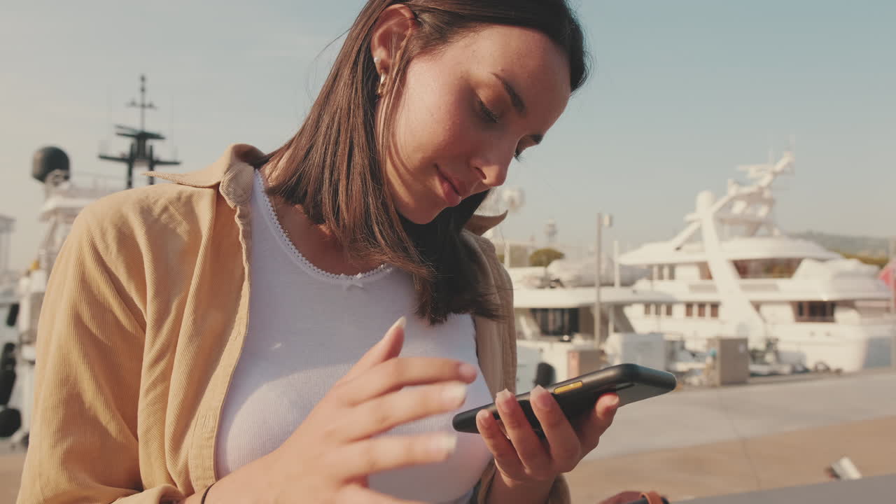 Young Woman Scrolling on Smartphone at a Sunny Marina
