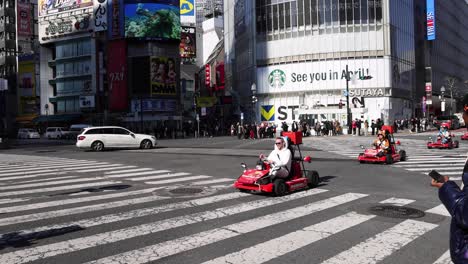 people in go-karts driving across a city intersection