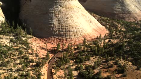 drone footage of an unusual rock formation, from top to bottom, with indiscernible vehicles moving along the road