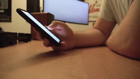 man scrolling through cell phone calendar at computer desk with moving screen saver in the background