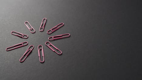 Close-up-of-pink-paper-clips-arranged-with-copy-space-on-black-background,-in-slow-motion