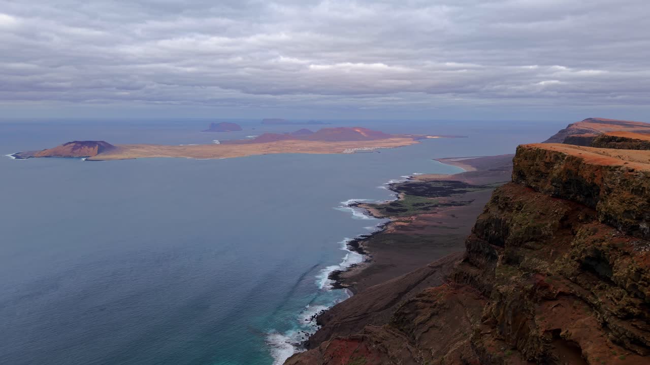This aerial shot showcases Mirador de Gayo in Lanzarote Canary Islands featuring a volcanic landscape meeting the ocean under a cloudy sky It's travel tourism and geological concepts