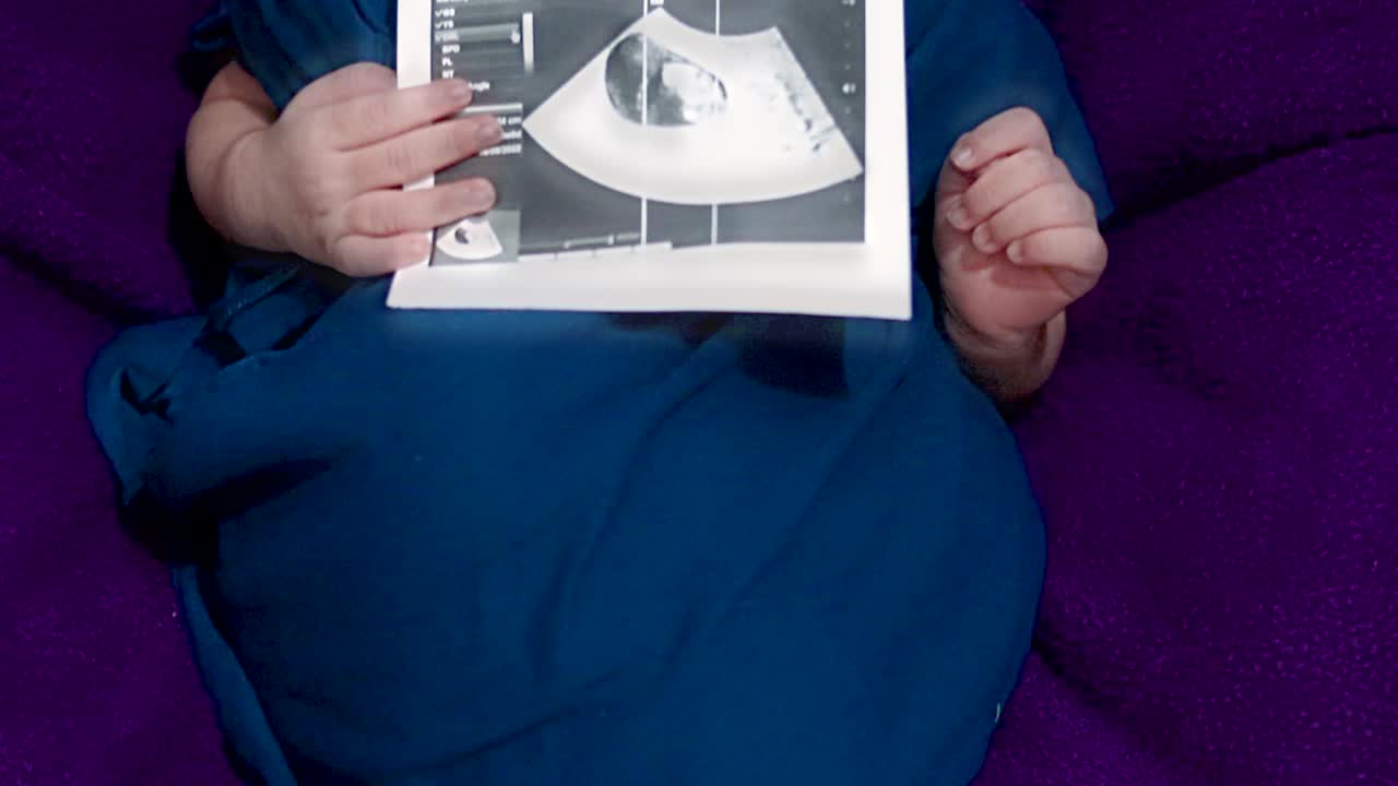newborn baby holding ultrasound copy in hand and sleeping at mother palm in baby wrap