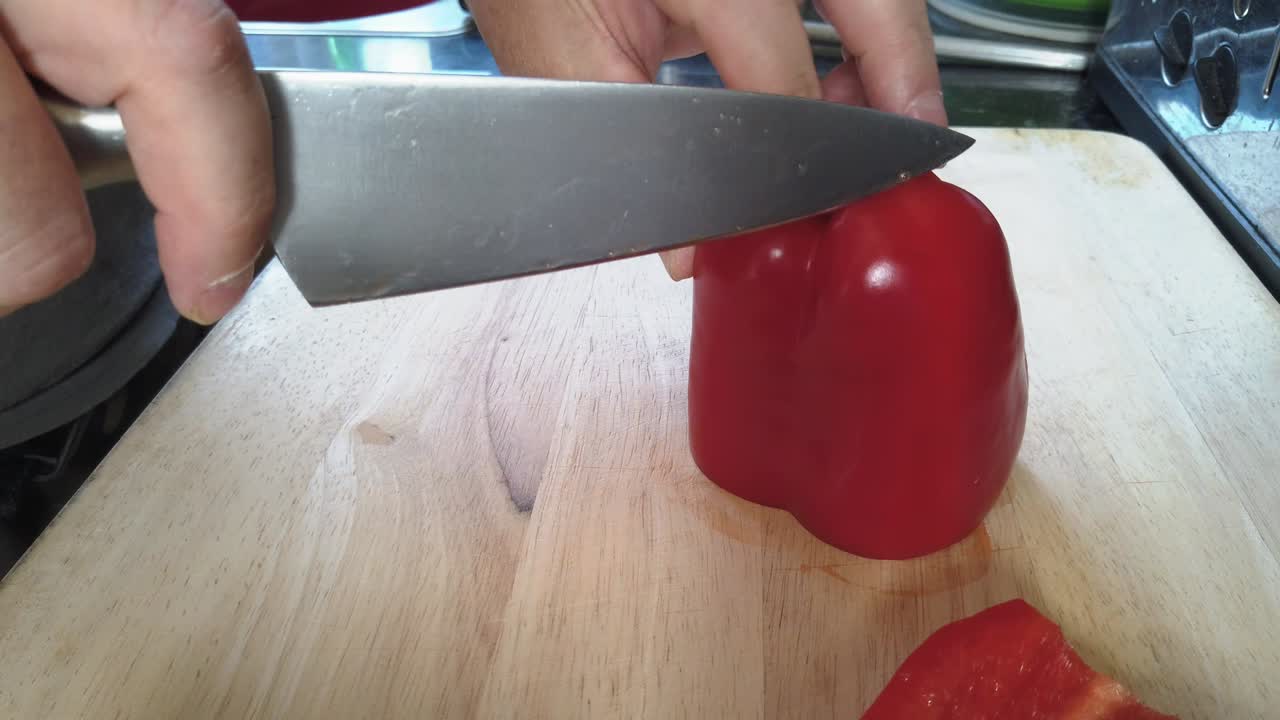 A man prepares fresh red bell peppers on a wooden chopping board at home