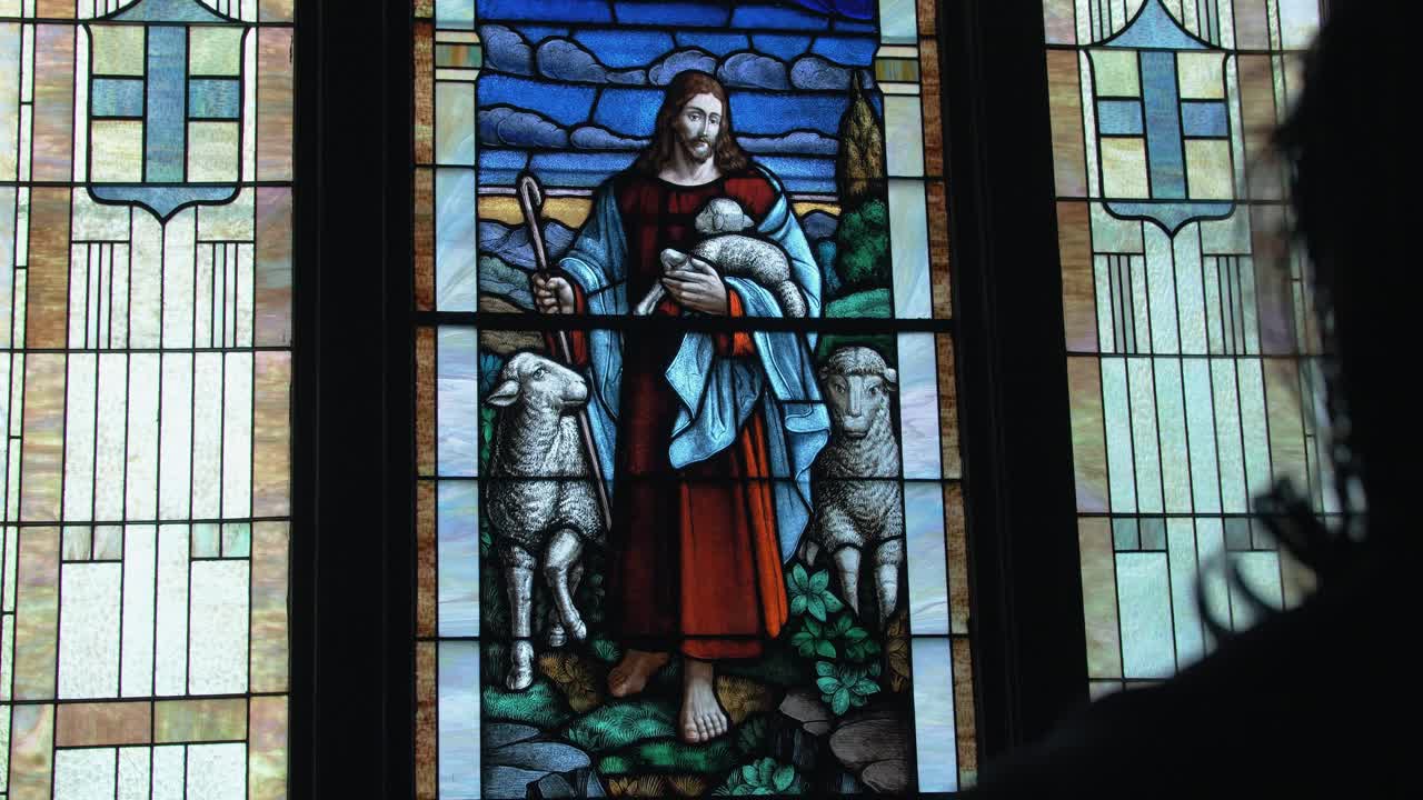 Back shot of Christian man, priest, preacher, pastor looking at stained glass window creating a cinematic and contemplative mood