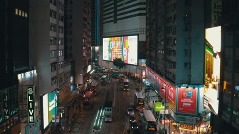 drone shot traveling upward in the middle of the city of hong kong in causway bay crossroad during the night. a huge screen display is on the facade of the building in the front.