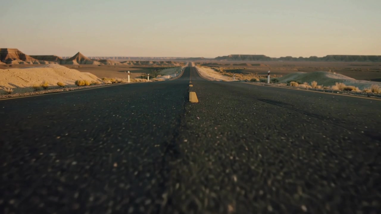 Una telecamera in movimento che avanza lentamente, stringendo la messa a fuoco su un'autostrada desertica asfaltata, evidenziando la linea gialla.