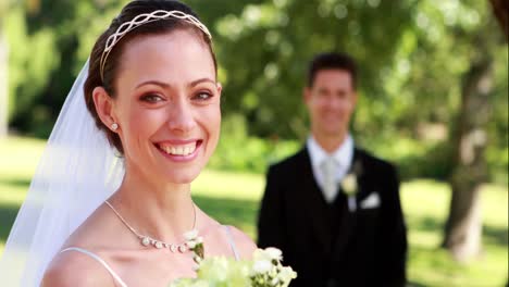 pretty bride smiling at camera with groom standing in background