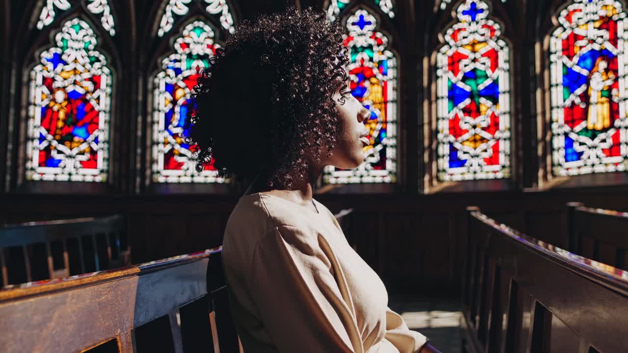 Side profile of a person seated in a church, illuminated by colorful stained glass