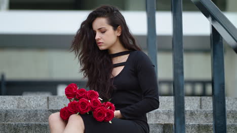 closeup woman sitting with flowers at street. woman throwing red roses on stairs