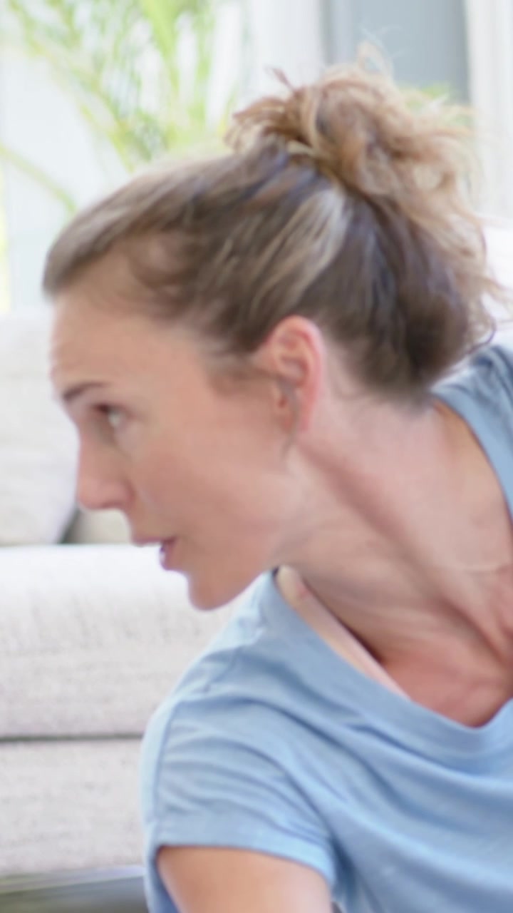 Video verticale: Istruttore in maglietta blu che si gira, guida un gruppo nello stretching di gambe e piedi a casa con tappetini.