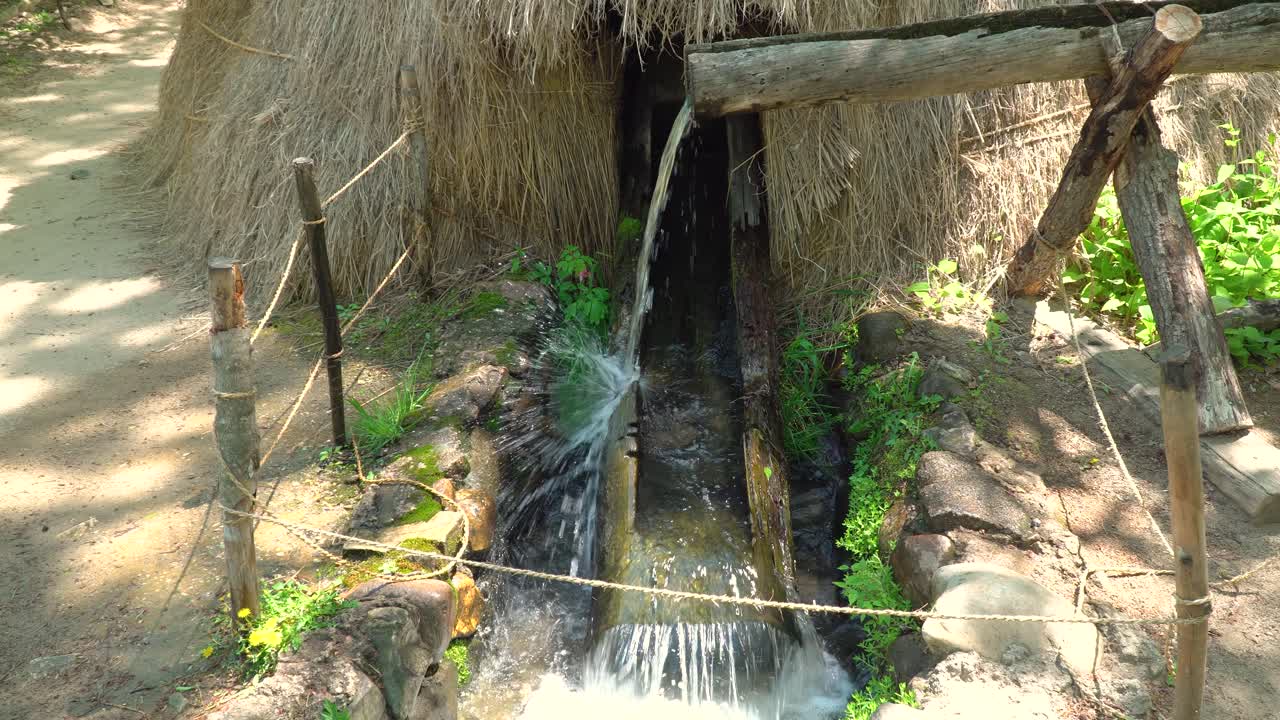 agua que fluye a través de tuberías de madera abiertas que llenan el molino de agua de madera para moler trigo y arroz en la aldea popular coreana de la ciudad de yongin, corea