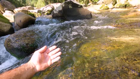 a man's hand moving in the stream of clean water from a waterfall