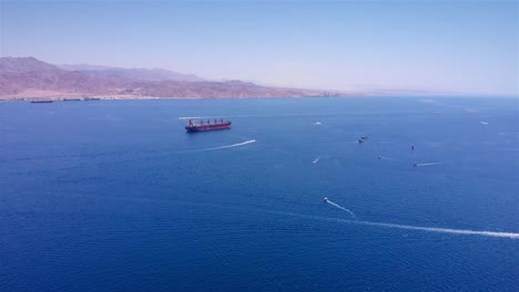 aerial view of a cargo ship and recreational boats in a vast bay with mountains in the background